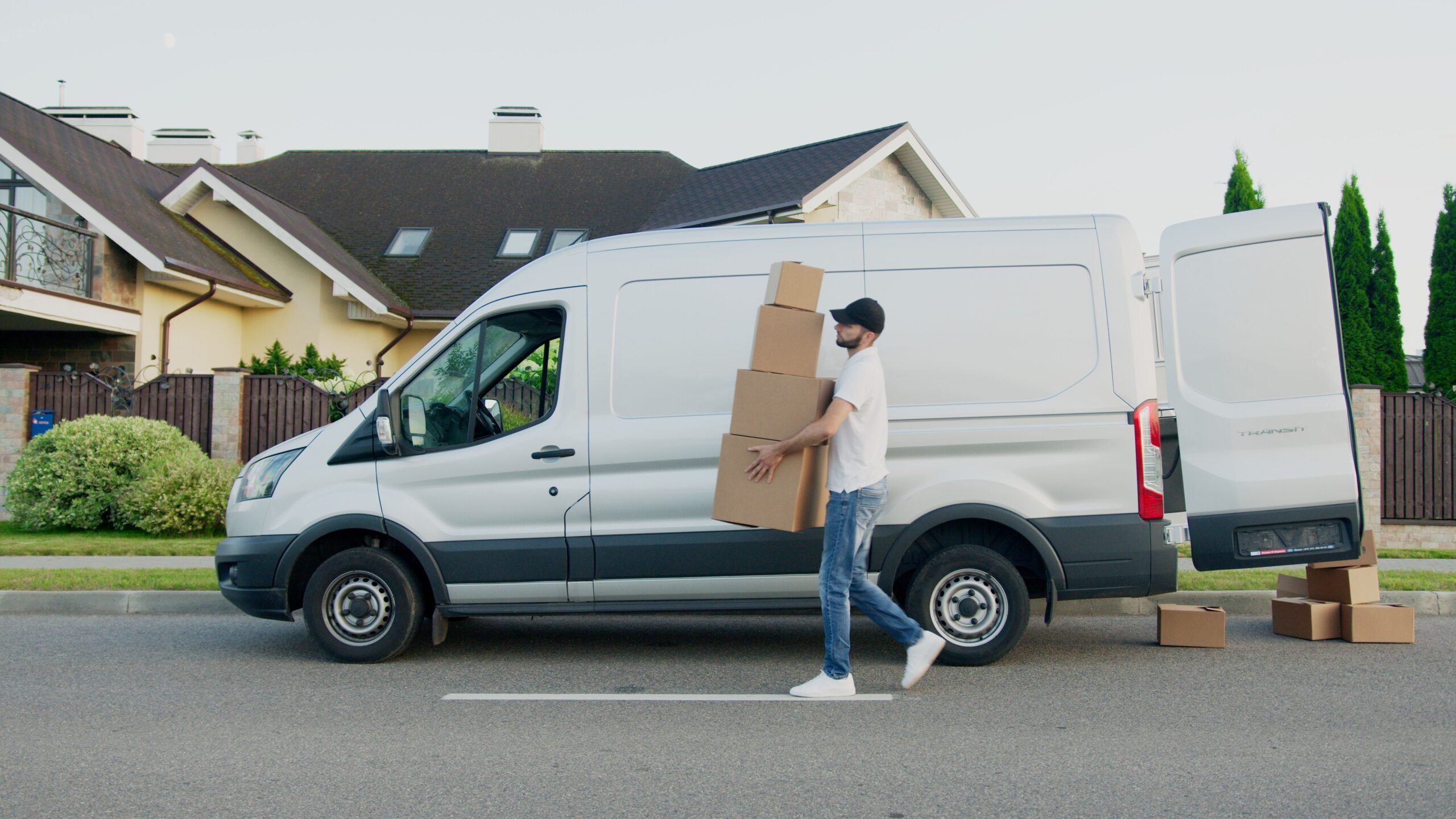 Services Man unloading cardboard boxes from a delivery van in a suburban neighborhood street.