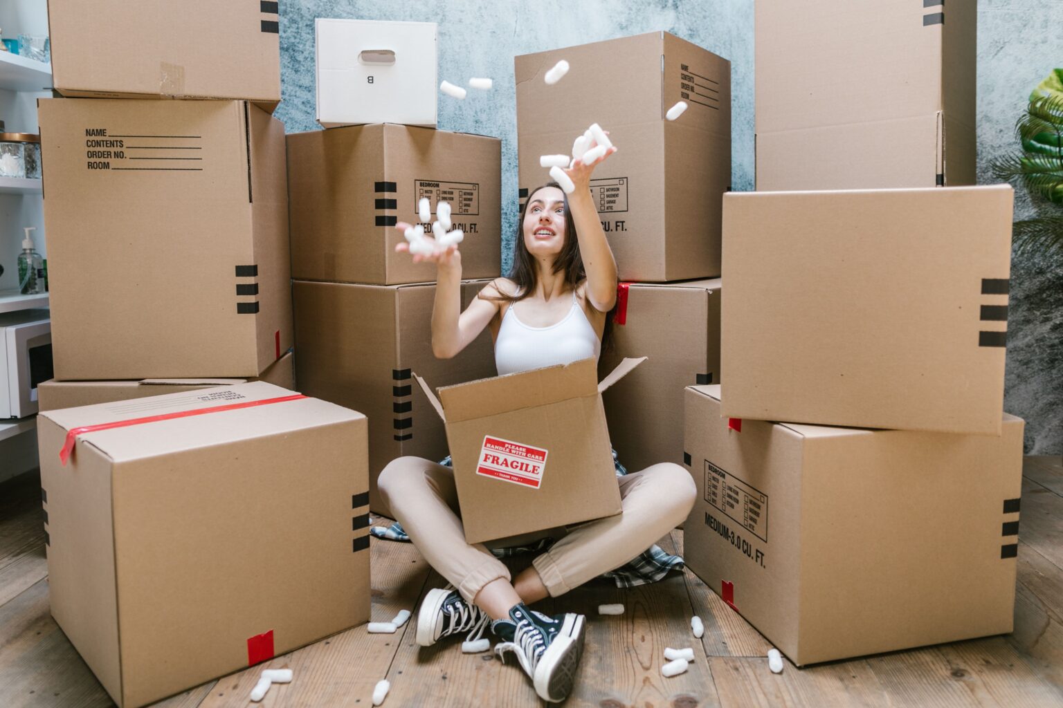 Services Young woman surrounded by cardboard boxes, happily moving into her new apartment.